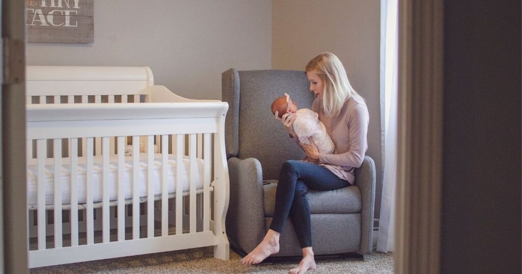 Mom holding her baby next to a baby cot mattress.