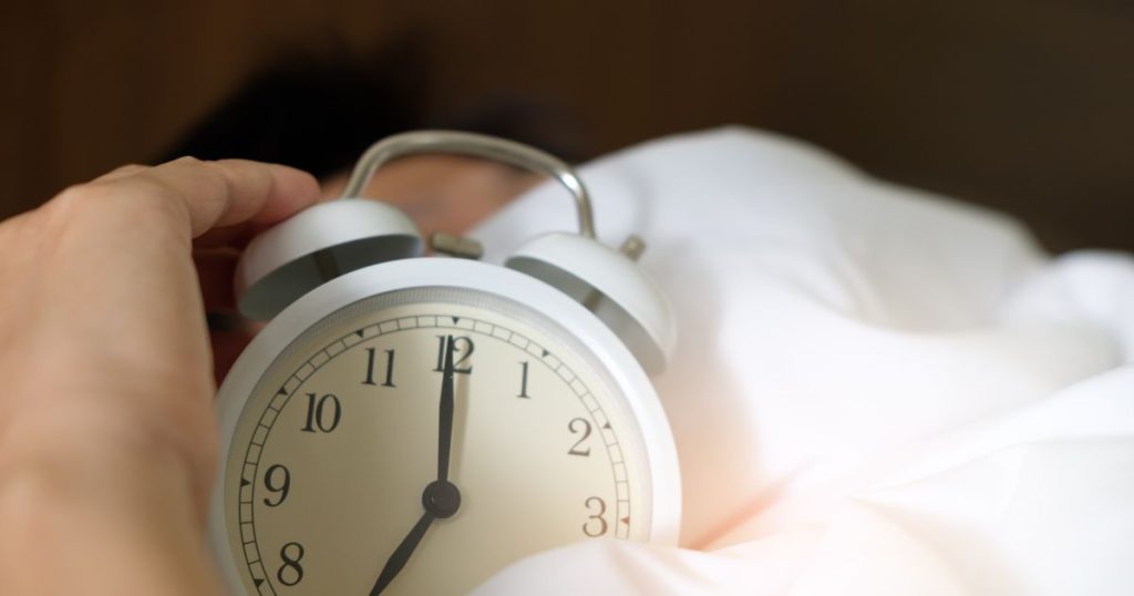 Person holding an alarm clock in bed.