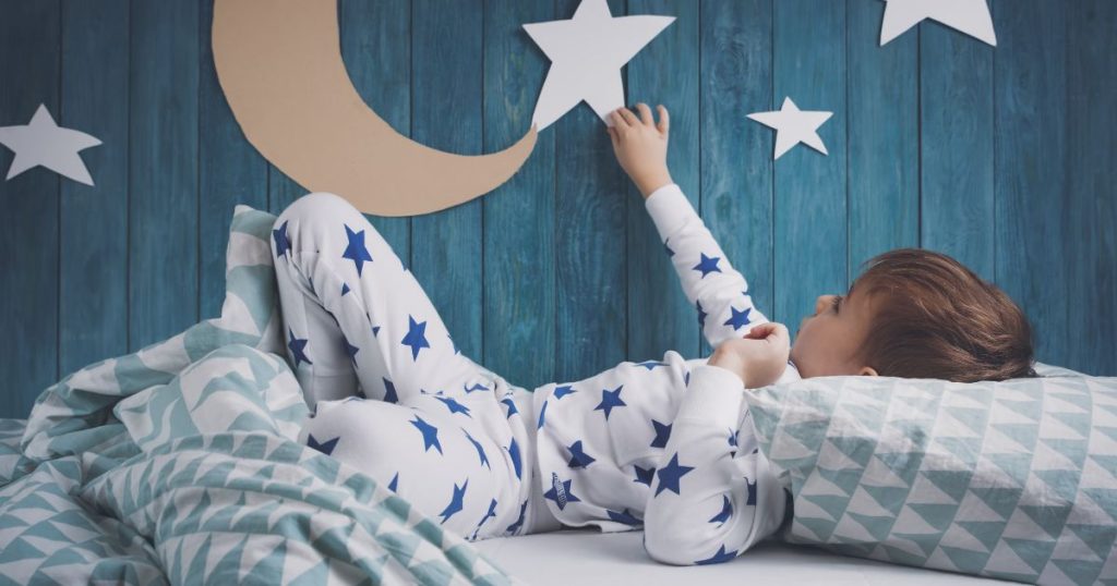 Little boy laying in bed while touching the wall decor in his bedroom.
