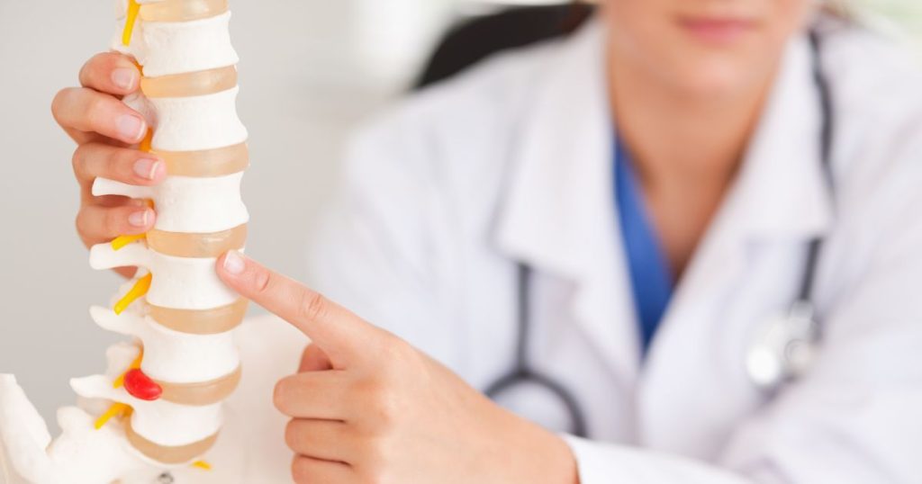 Doctor pointing at anatomy model of the spine to show possible causes of back pain.