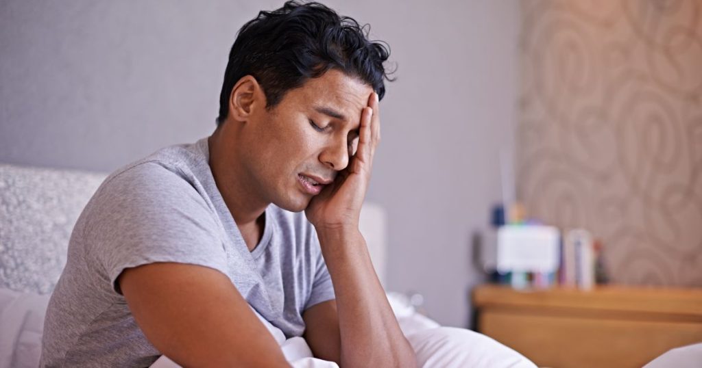 Man not feeeling well in the morning due to sleeping on a sagging mattress