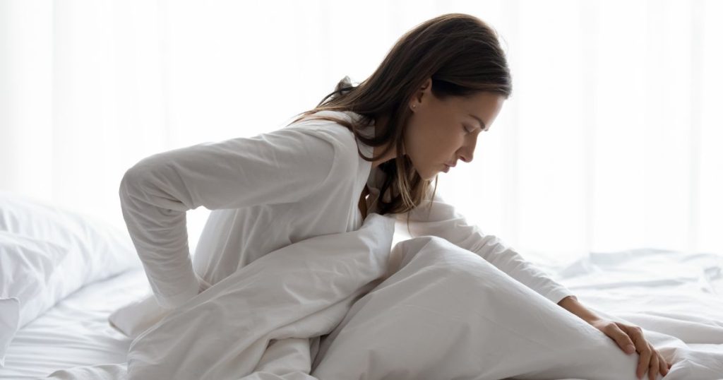 Woman holding her back in pain as she sits up in bed