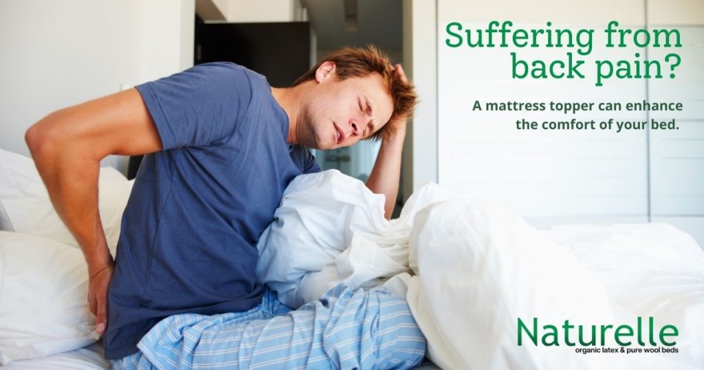 Image of a man holding his lower back in pain with text overlay "suffering from back pain? A mattress topper can enhance the comfort of your bed."